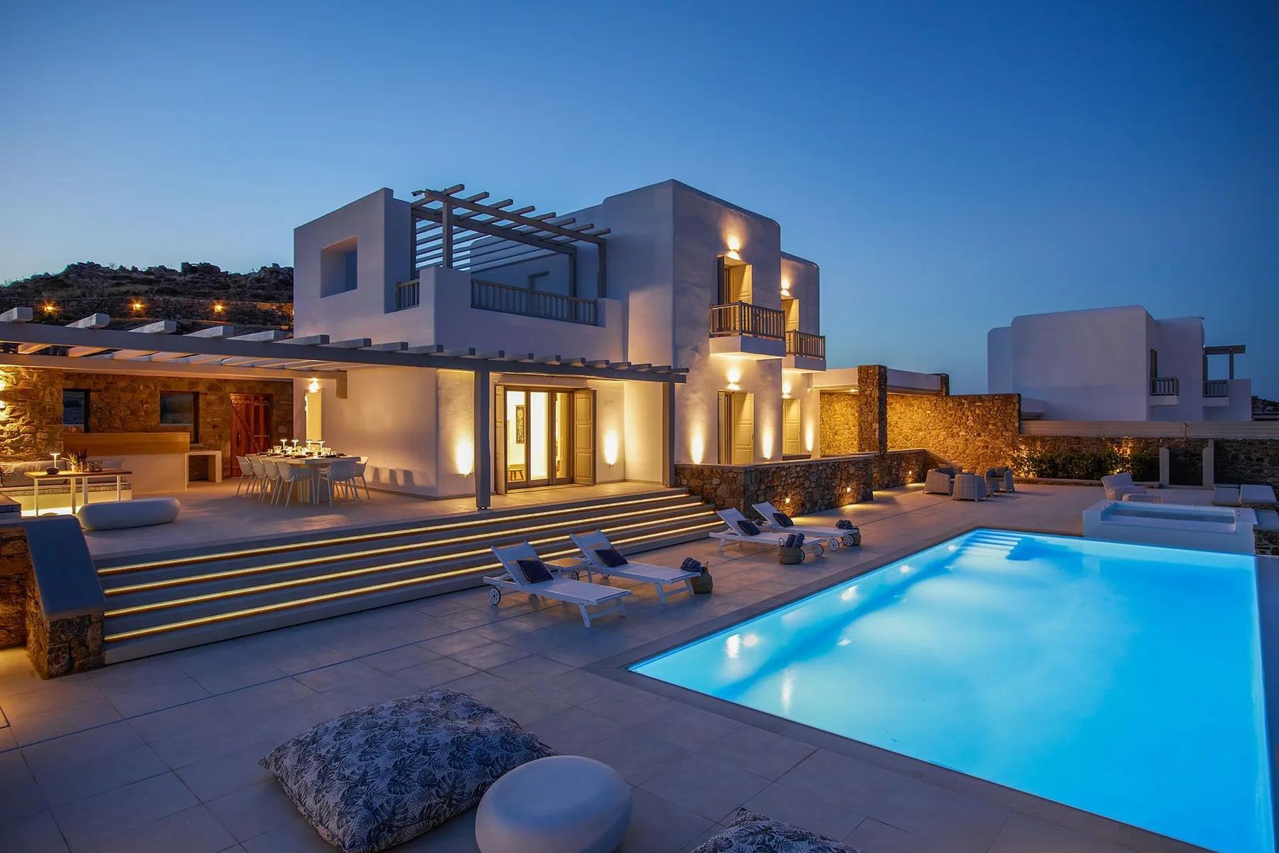 A modern house opens onto a lit swimming pool and outdoor seating area.