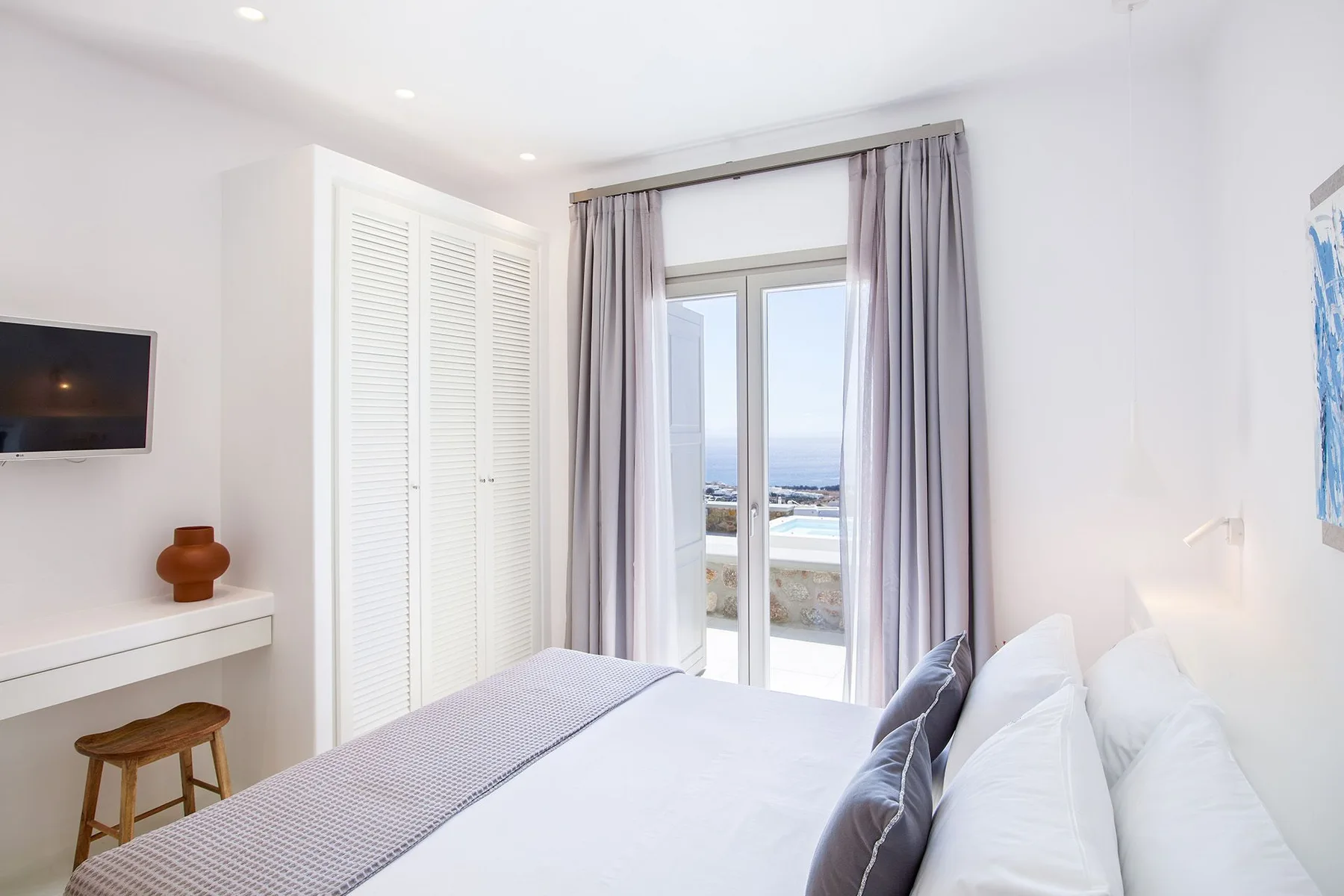 A bright bedroom with a bed beside glass doors opening onto a balcony.