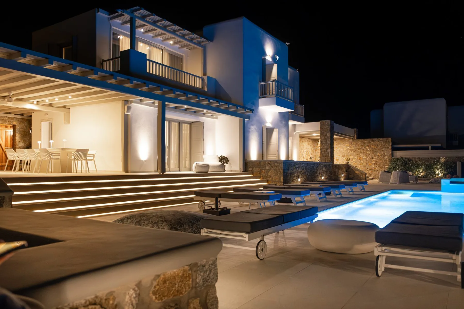 A modern house with a lit swimming pool and outdoor seating at night.