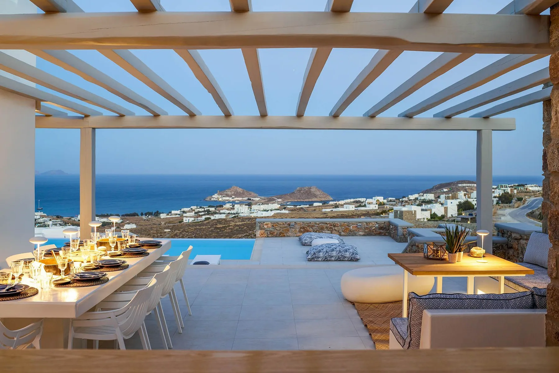 An outdoor dining and lounge terrace overlooks the sea beneath a wooden pergola.