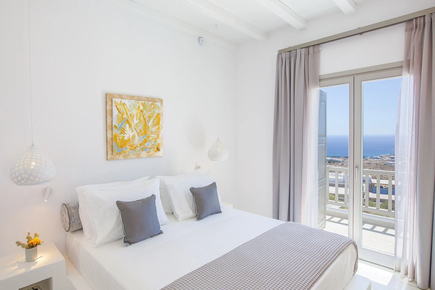 A bright bedroom with a bed beside glass doors opening onto a balcony.