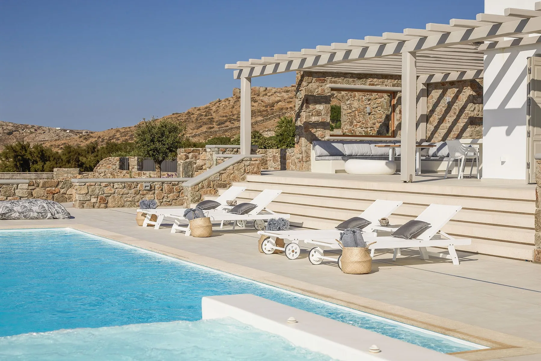 An outdoor pool beside a sun deck with lounge seating and a shaded terrace.