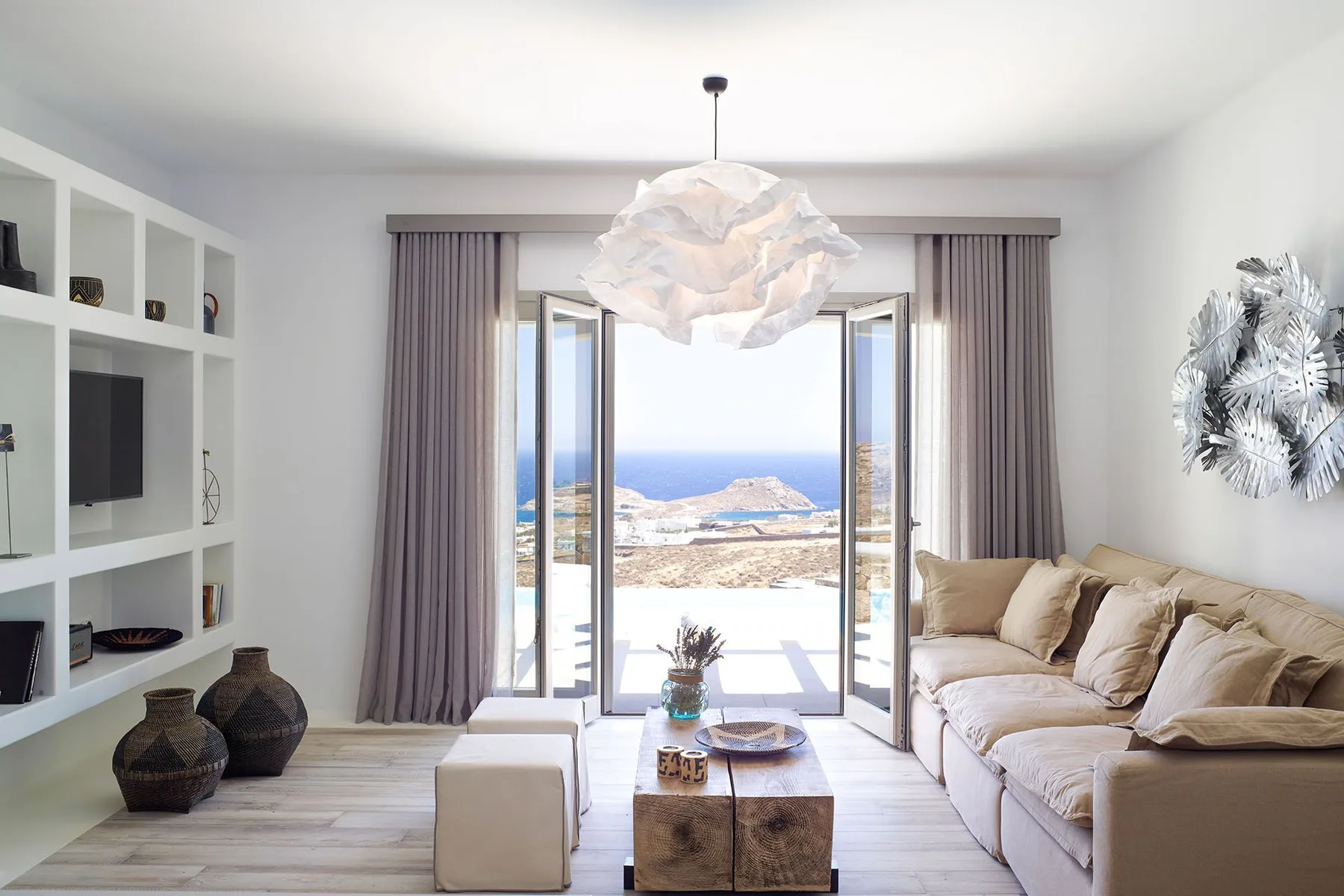 A bright living room with seating and open doors overlooking the sea.