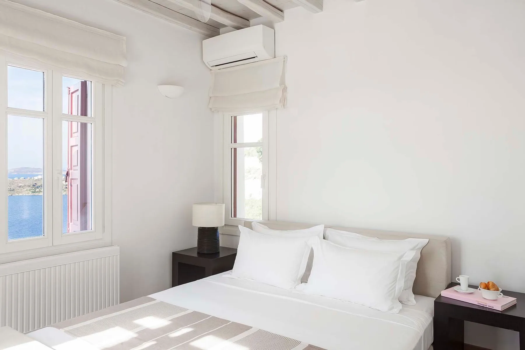Un dormitorio luminoso con una cama bien hecha y ventanas con vistas al agua.