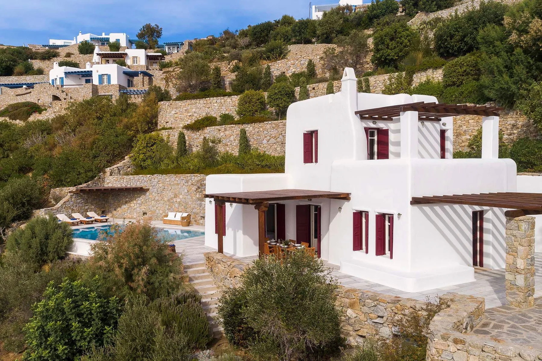 Una villa blanca en la ladera tiene una terraza con vistas a una pequeña piscina.