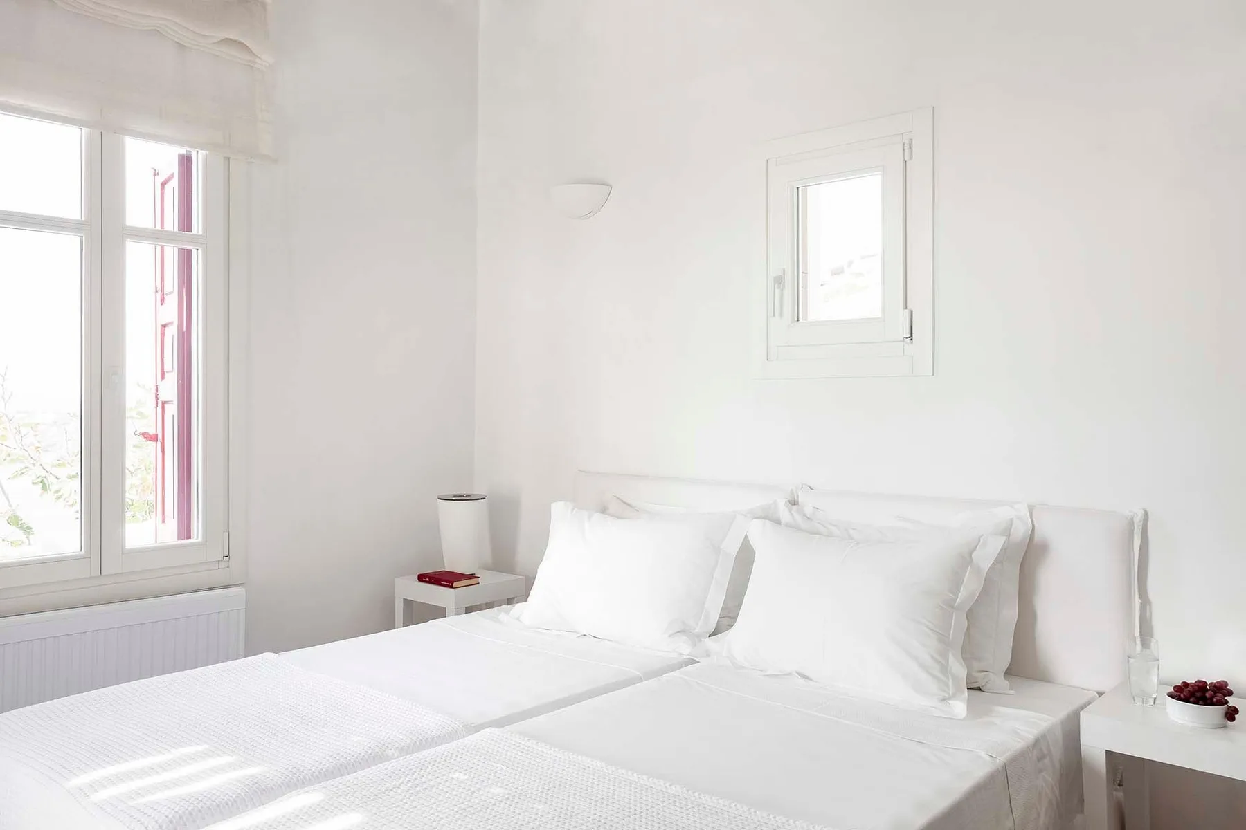 Un dormitorio luminoso con ropa de cama blanca y ventanas grandes.