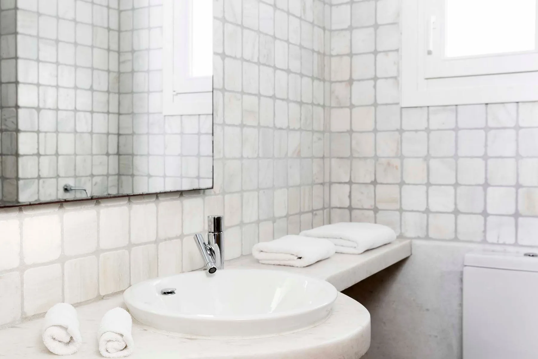 Lavabo de baño con un fregadero redondo, toallas dobladas y paredes de azulejos.