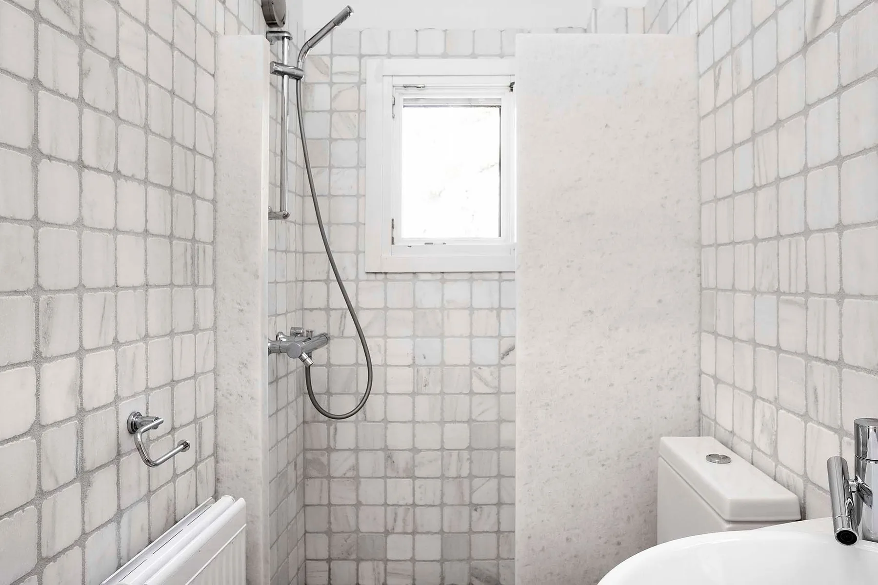 Un baño alicatado con ducha, ventana pequeña y lavabo.