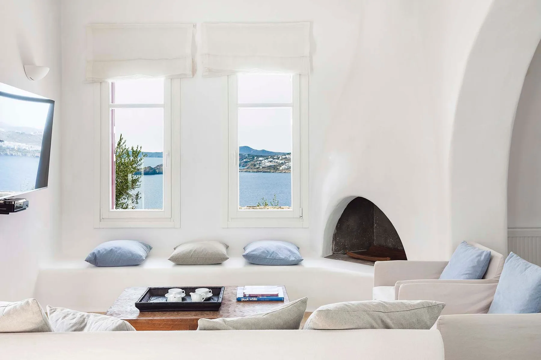 Una sala luminosa con zona de estar, dos ventanas y una chimenea empotrada.