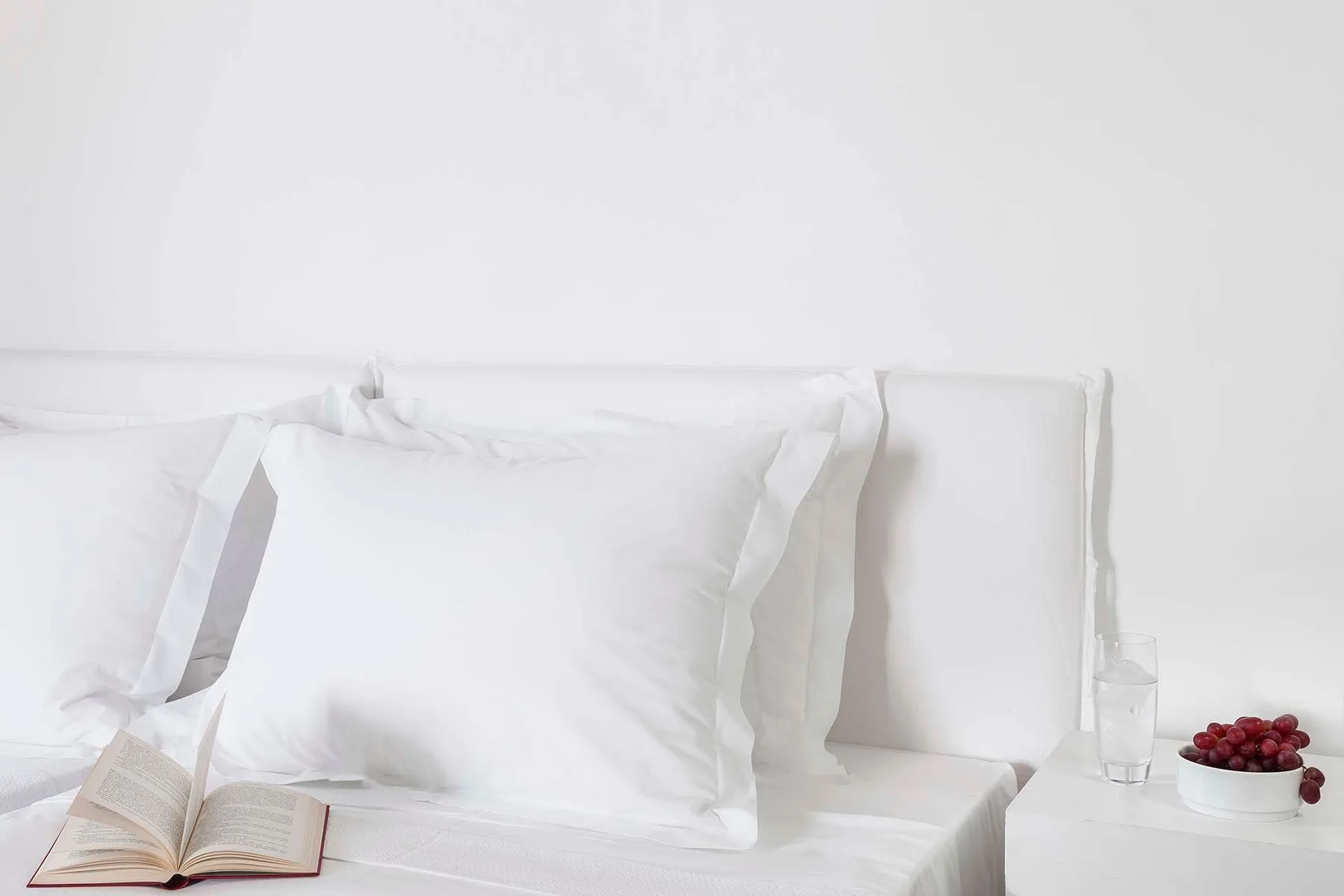 Un dormitorio luminoso con almohadas blancas y un libro abierto sobre la cama.
