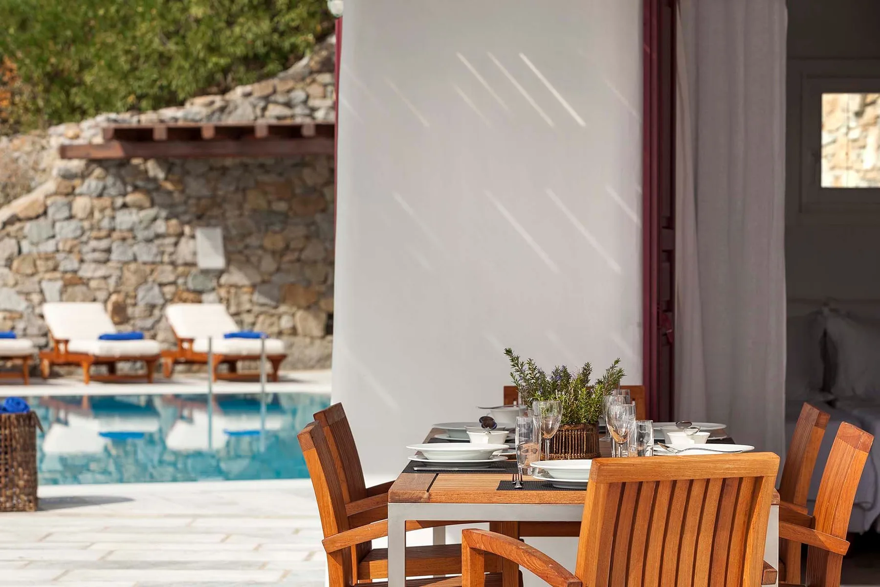 Una zona de comedor al aire libre con asientos de madera y una piscina junto a un muro de piedra.