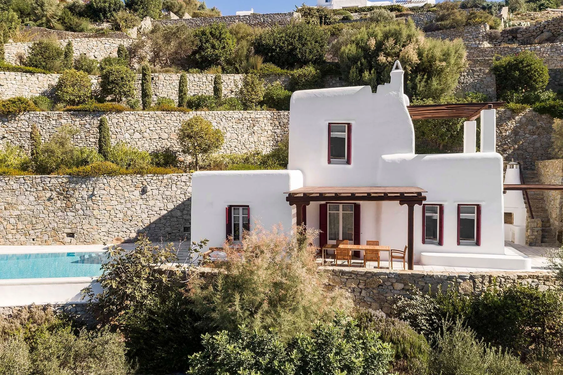 Una casa blanca se encuentra entre terrazas de piedra, con una piscina al frente.