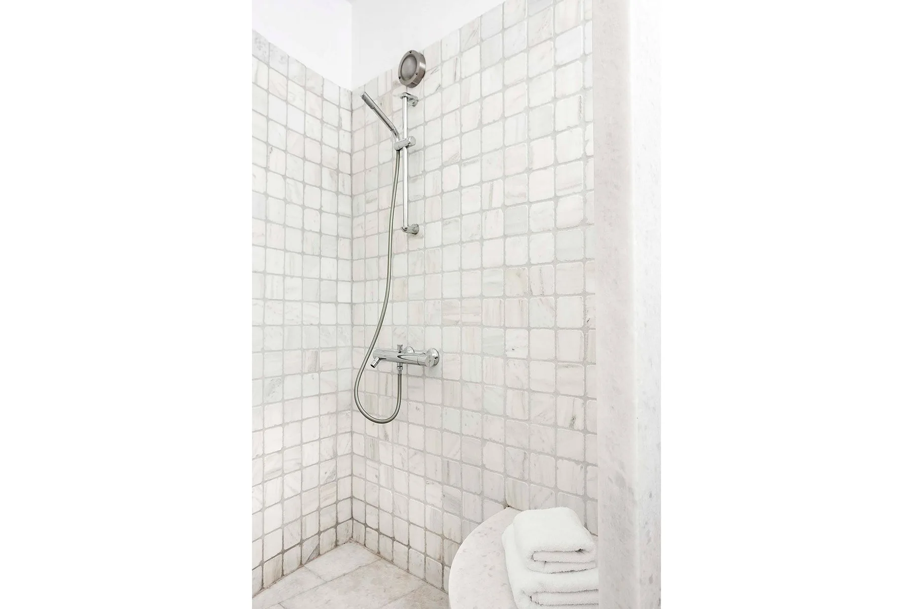 Una ducha de baño con azulejos, ducha de mano y toallas dobladas cerca.