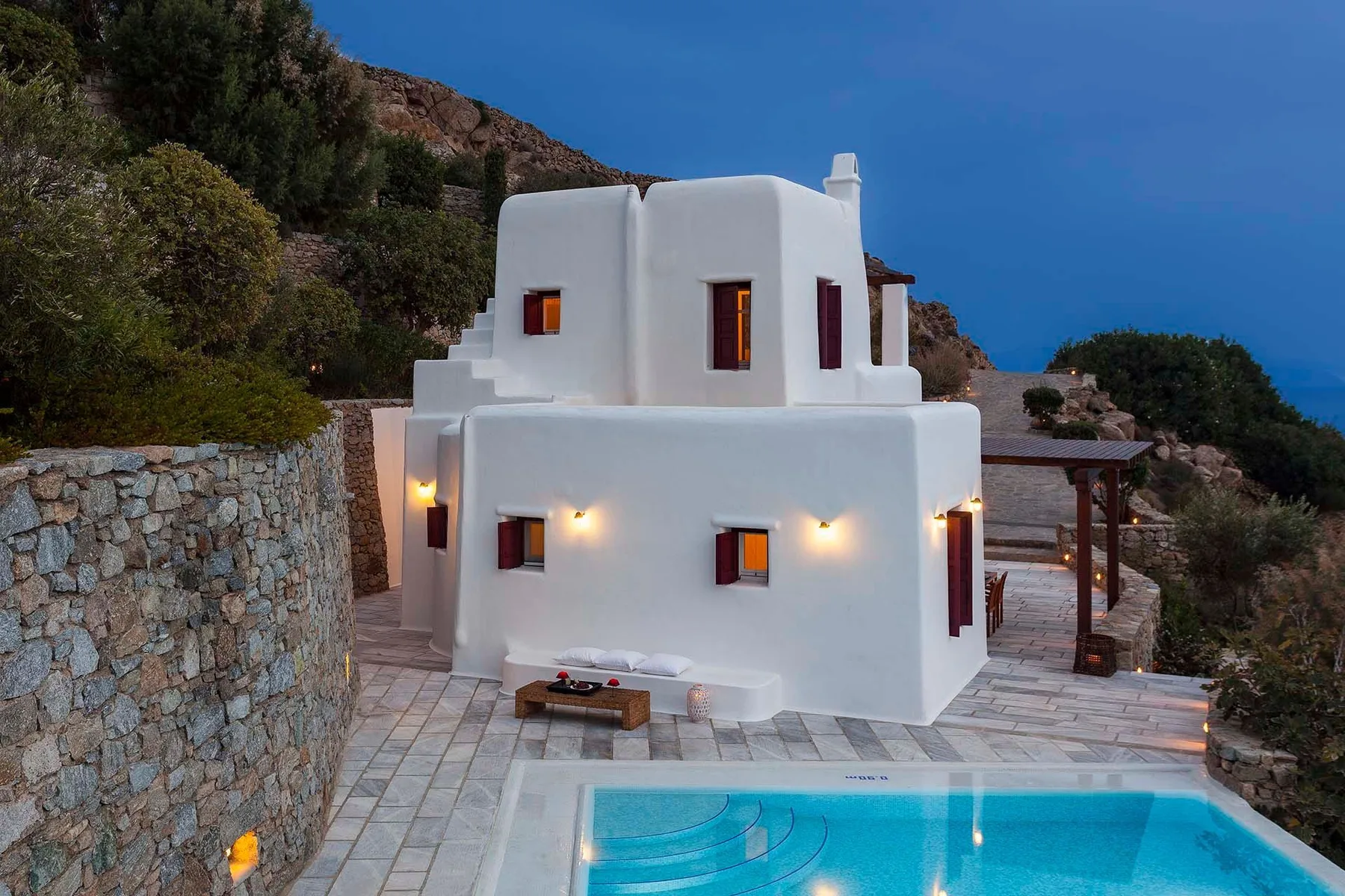 Una villa blanca junto a una piscina en una ladera rocosa.