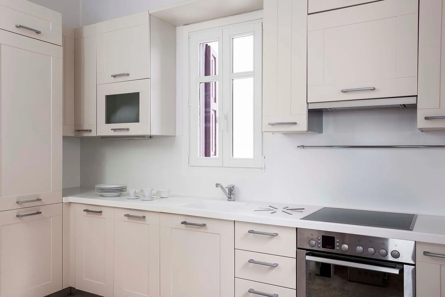 Una cocina luminosa con armarios blancos, una ventana y una placa eléctrica.