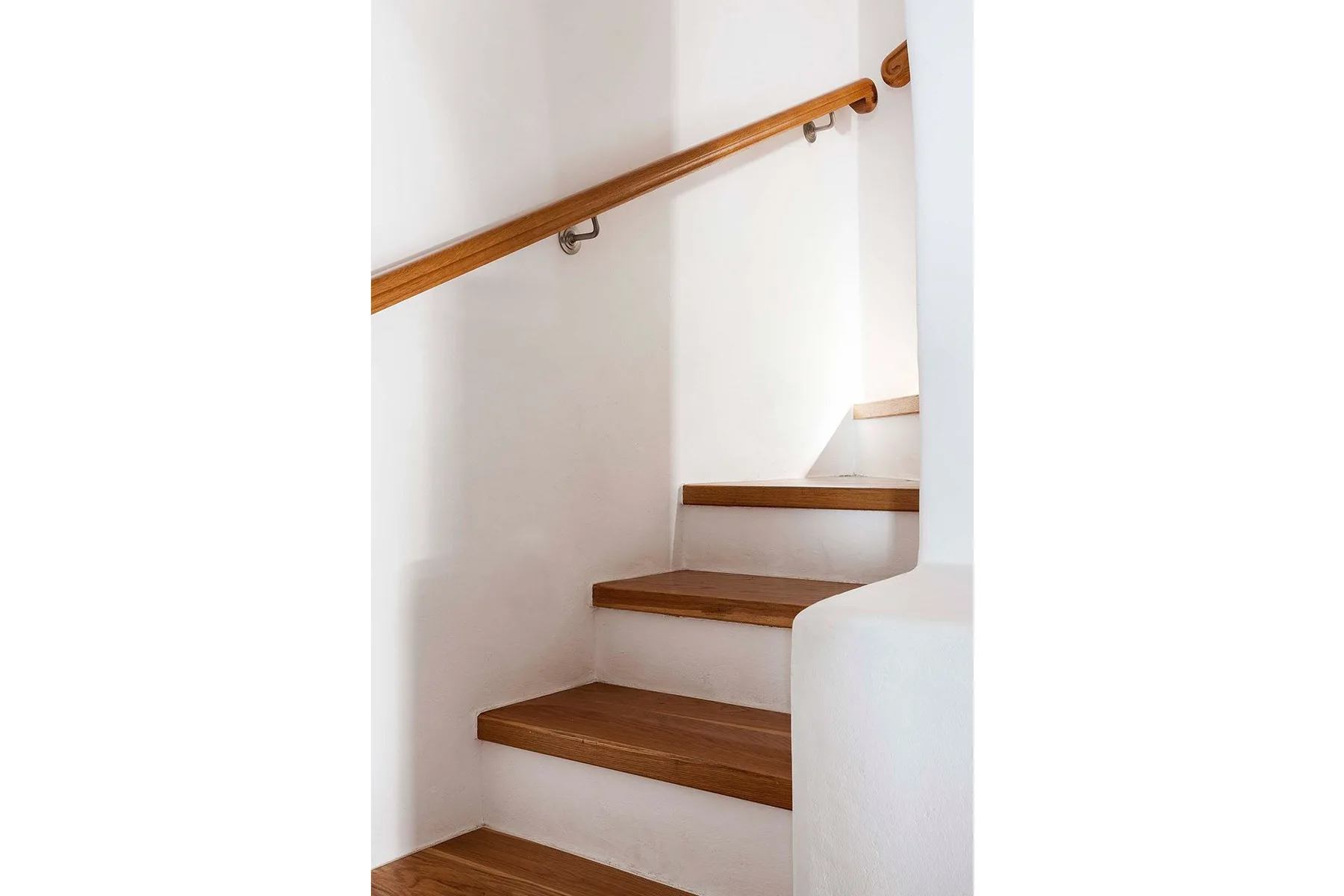 Una escalera interior blanca con peldaños y pasamanos de madera.