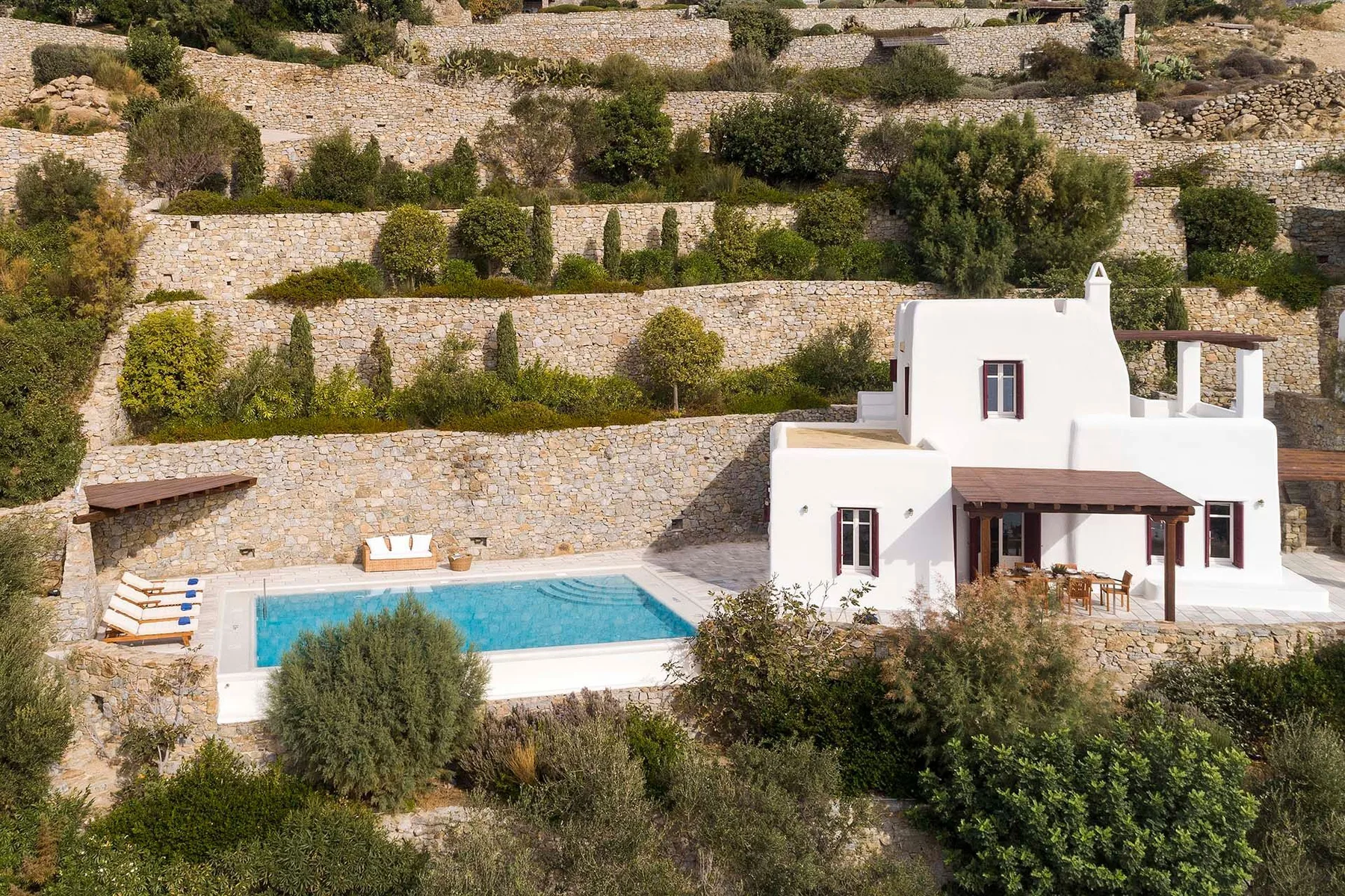 Una casa blanca está junto a una piscina, con terrazas de piedra en la ladera.
