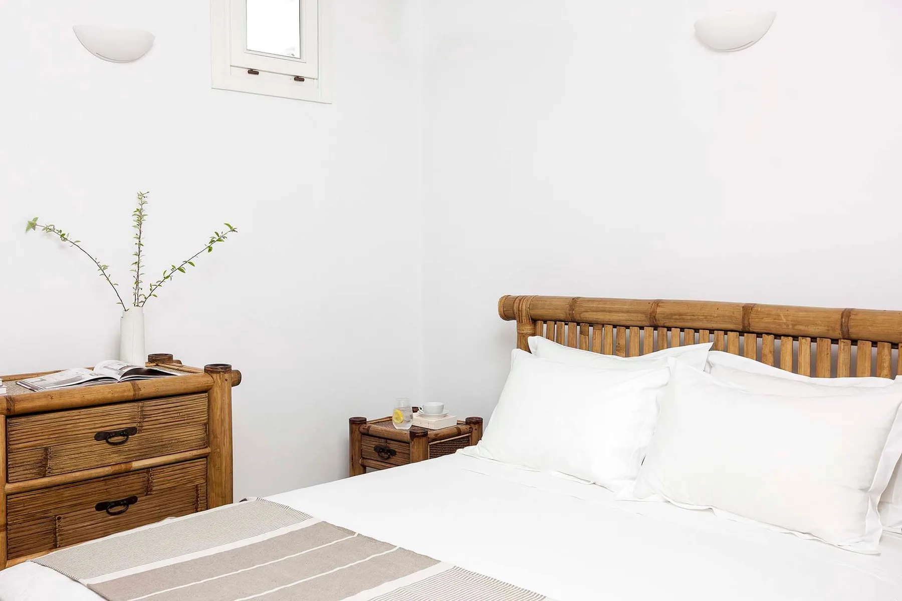 Un dormitorio con una cama, ropa de cama blanca y una mesita de noche de madera.