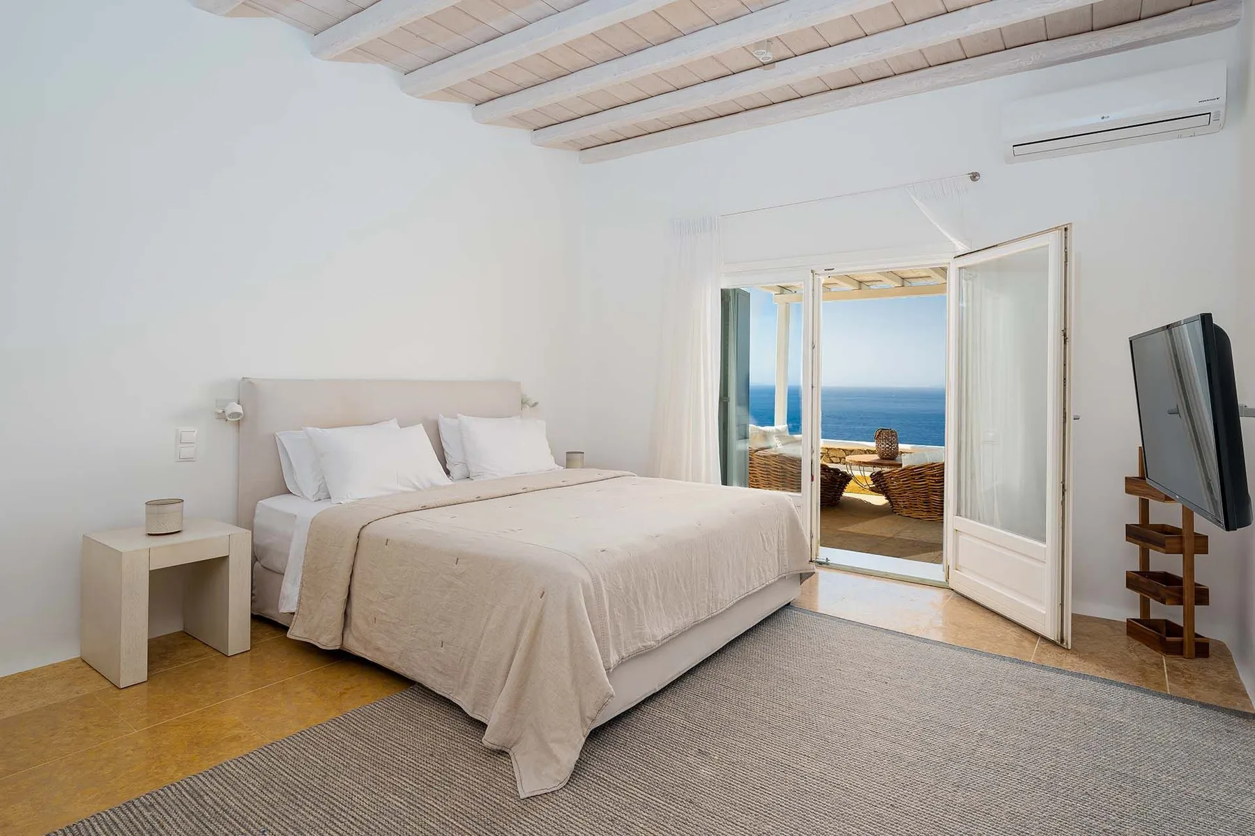 A bright bedroom with a bed and open doors overlooking the sea.