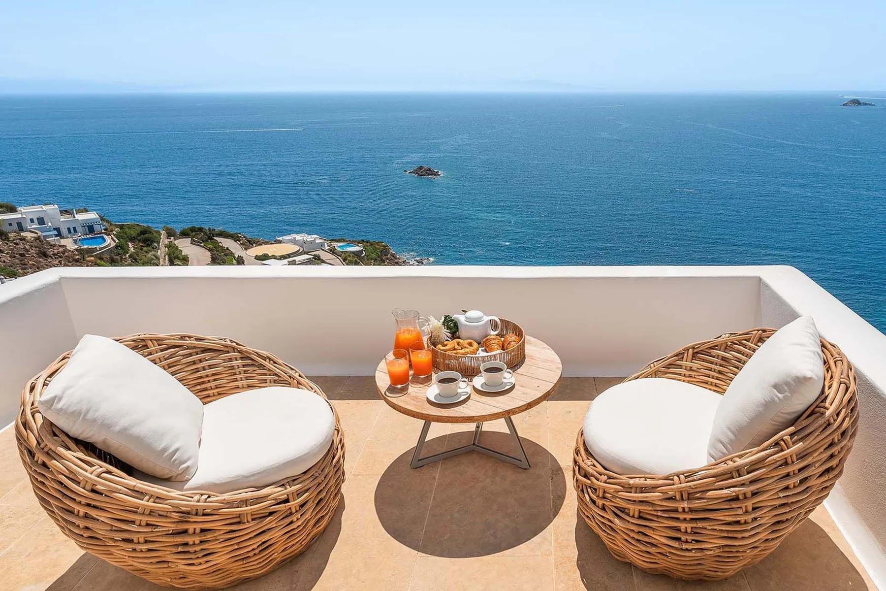 Two wicker seats and a small table sit on a terrace overlooking the sea.
