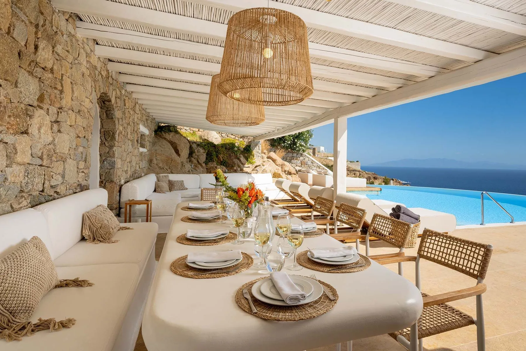 A covered outdoor dining area opens onto a blue swimming pool and sea view.