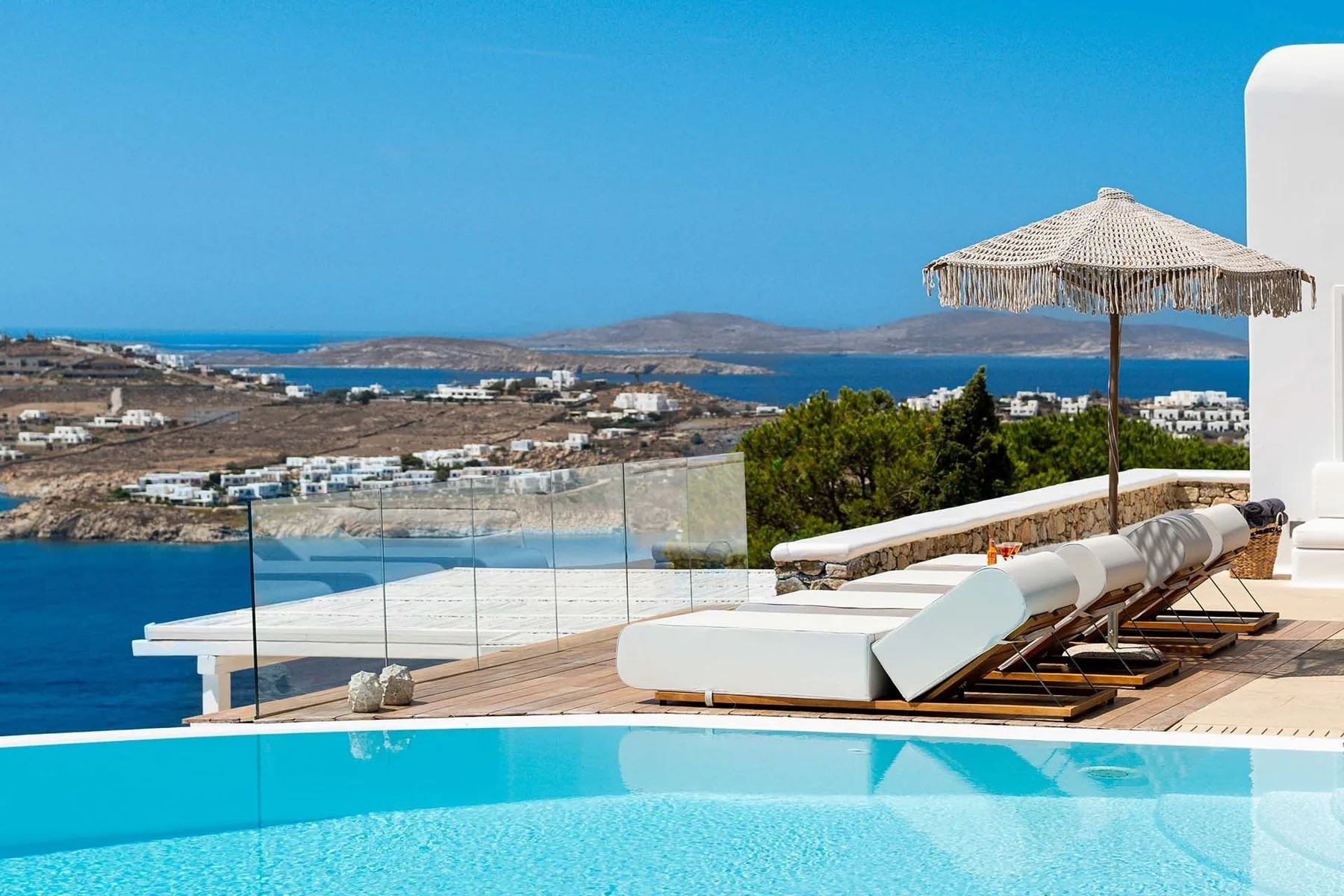 A seaside terrace with a swimming pool, lounge seating, and views of the coastline.