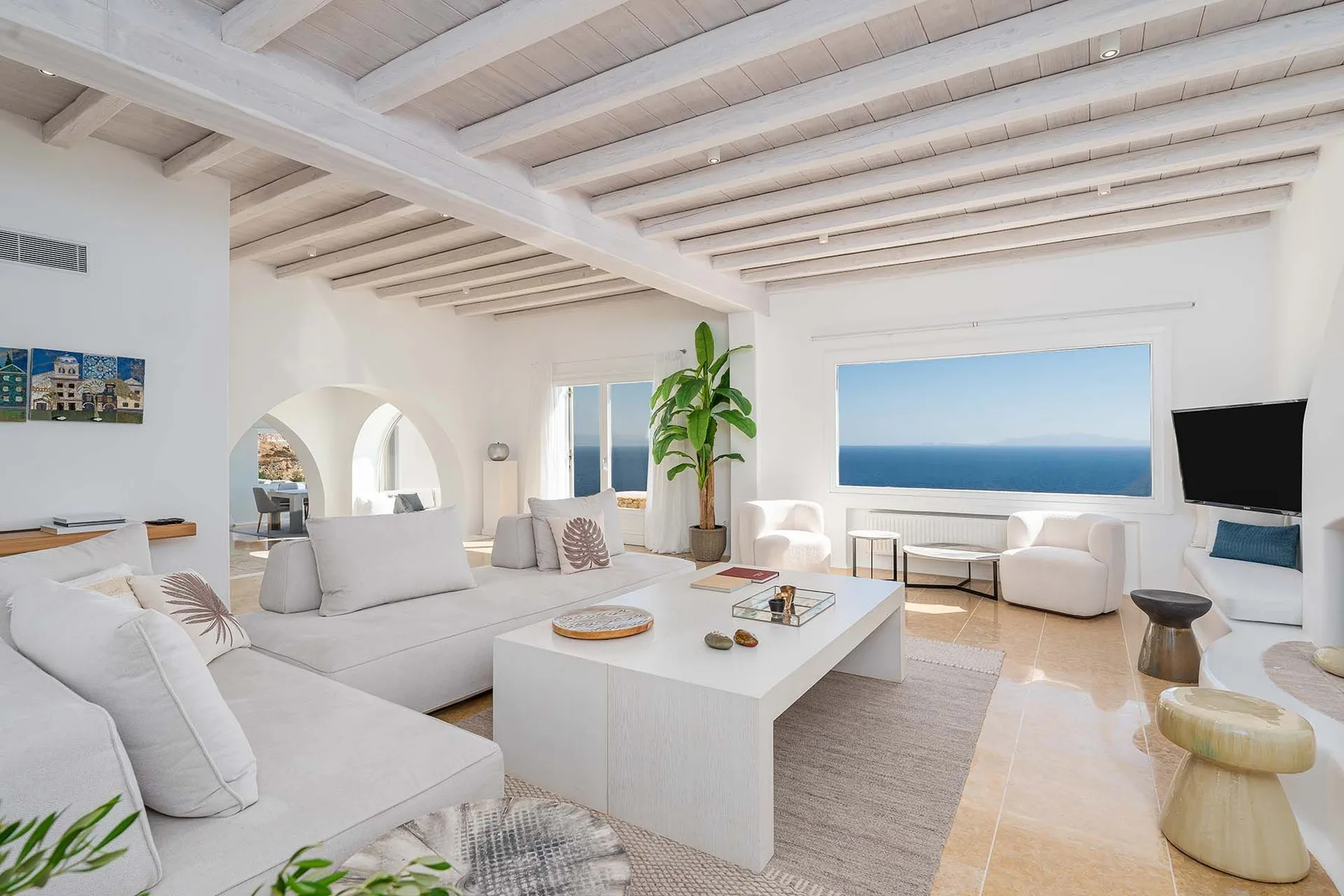 A bright living room with white seating, a coffee table, and a large ocean view.