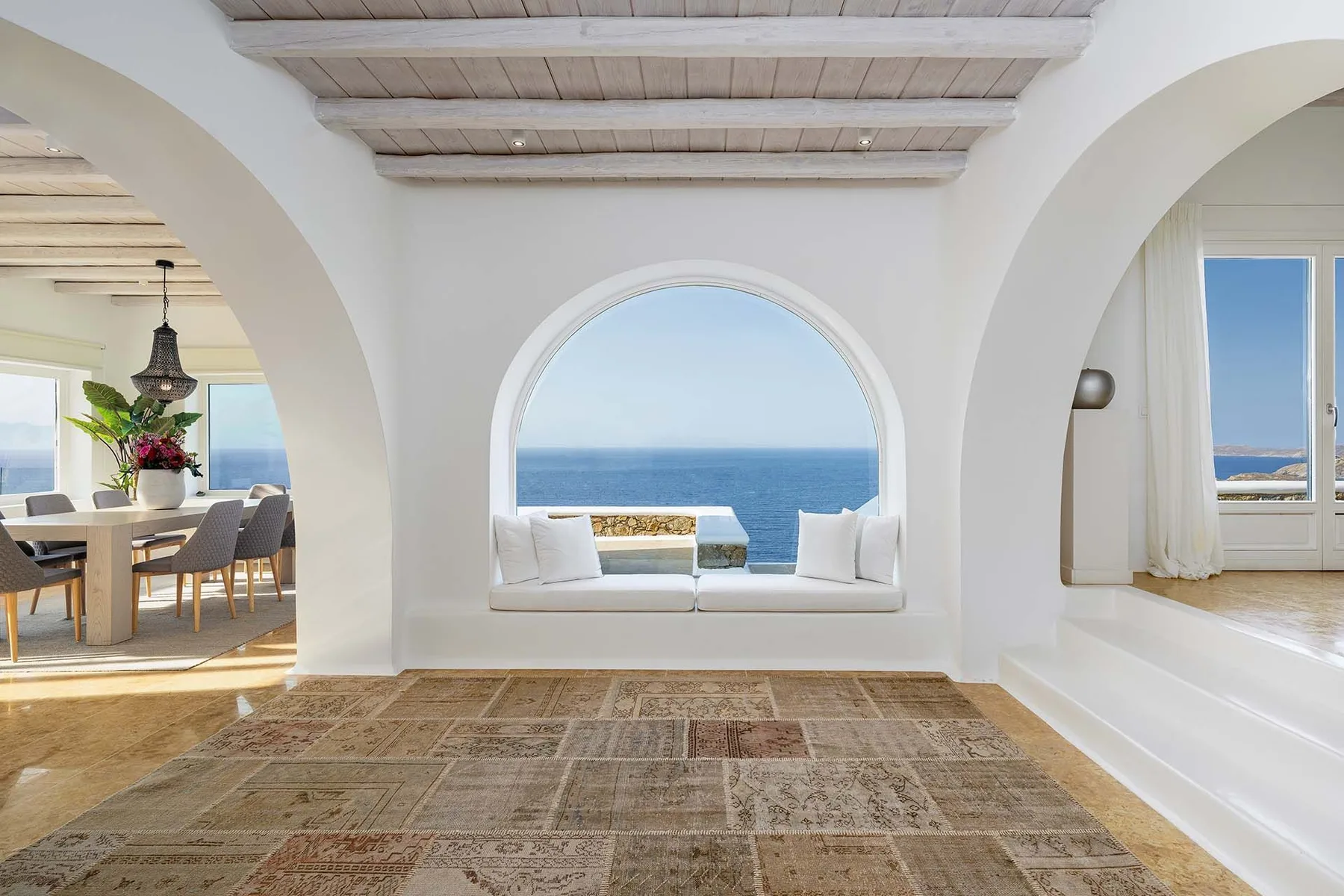 A bright living area with a large arched window overlooking the sea.