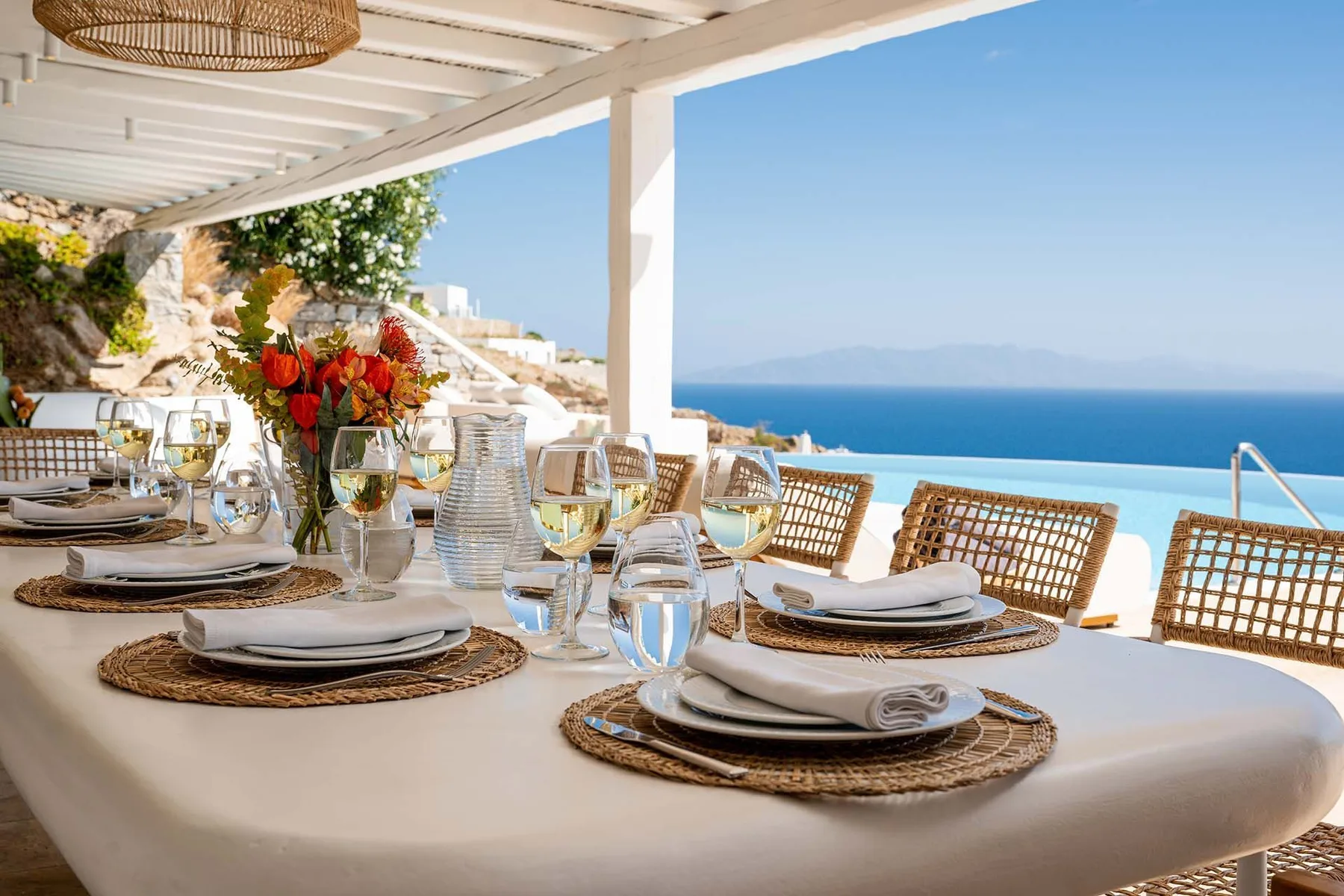 A set dining table sits on a covered terrace overlooking the sea.