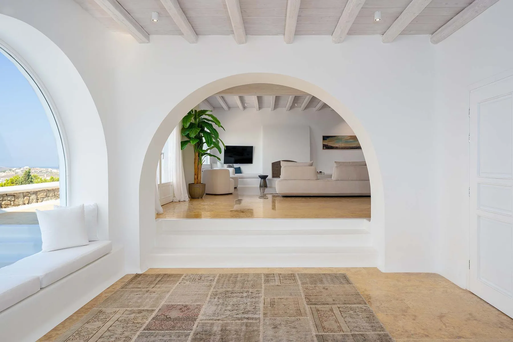 A bright living room is visible through an arched opening, with seating and a potted plant.
