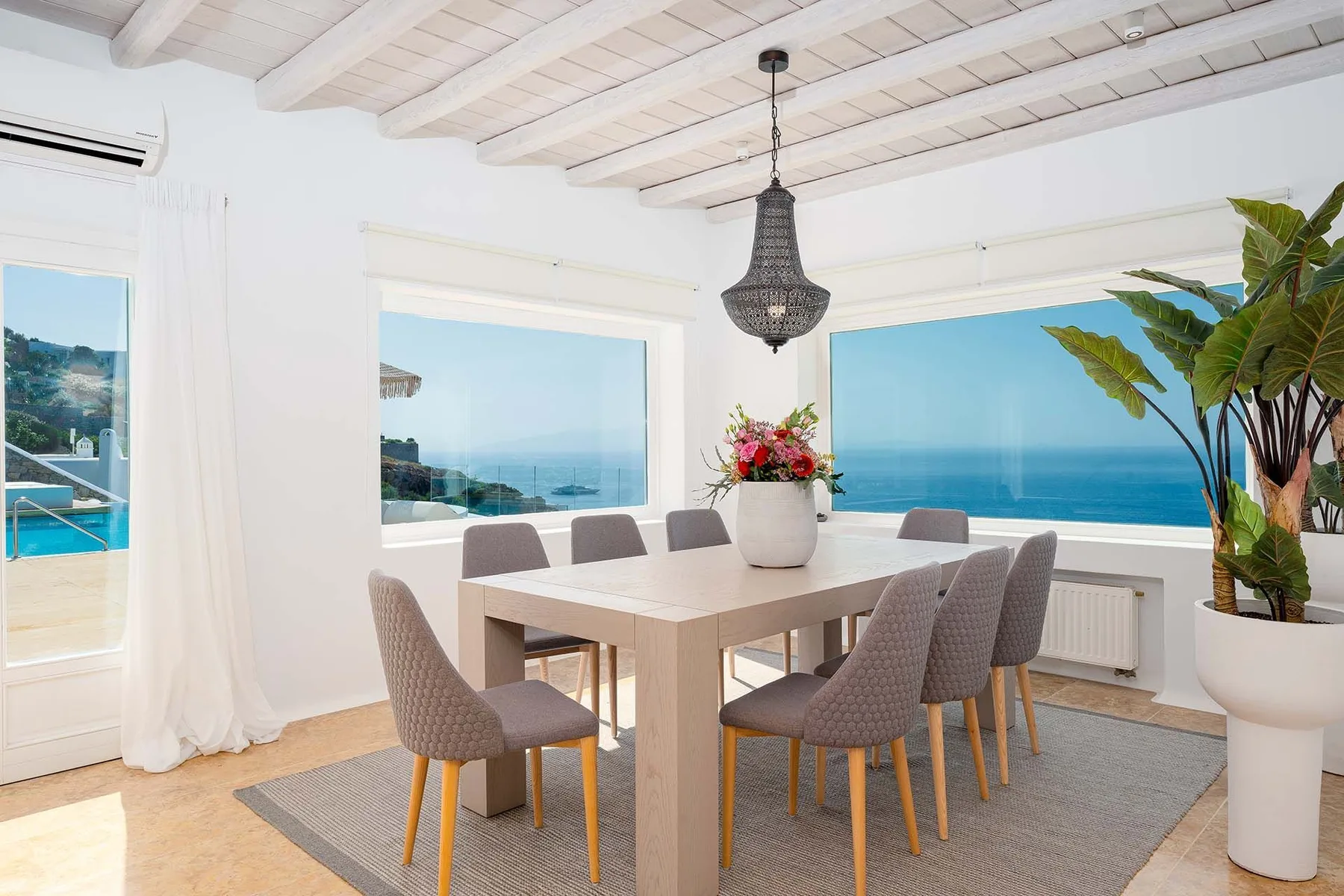 A dining area with a table and chairs beside large windows overlooking the sea.