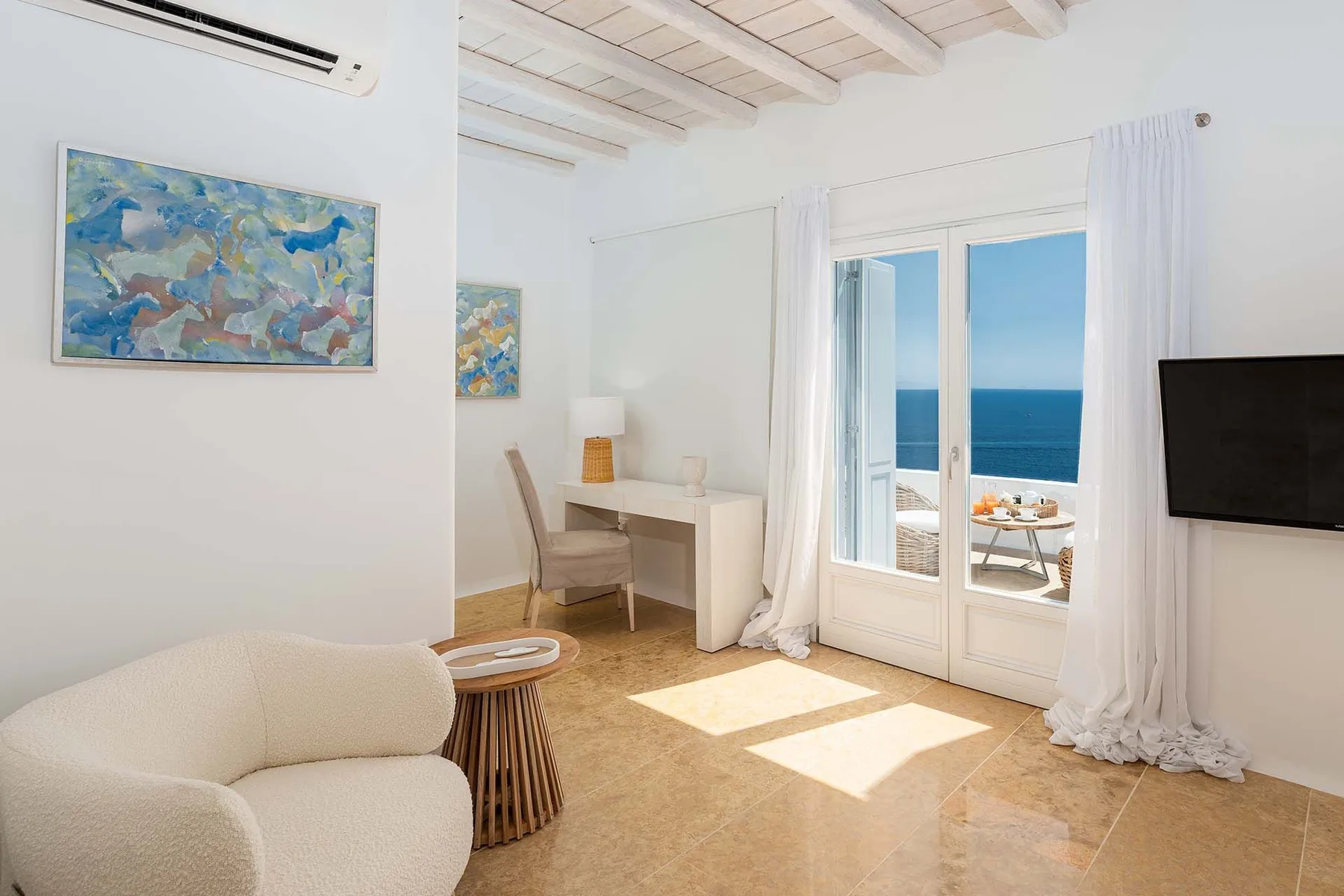 A bright living room with an armchair and glass doors overlooking the sea.