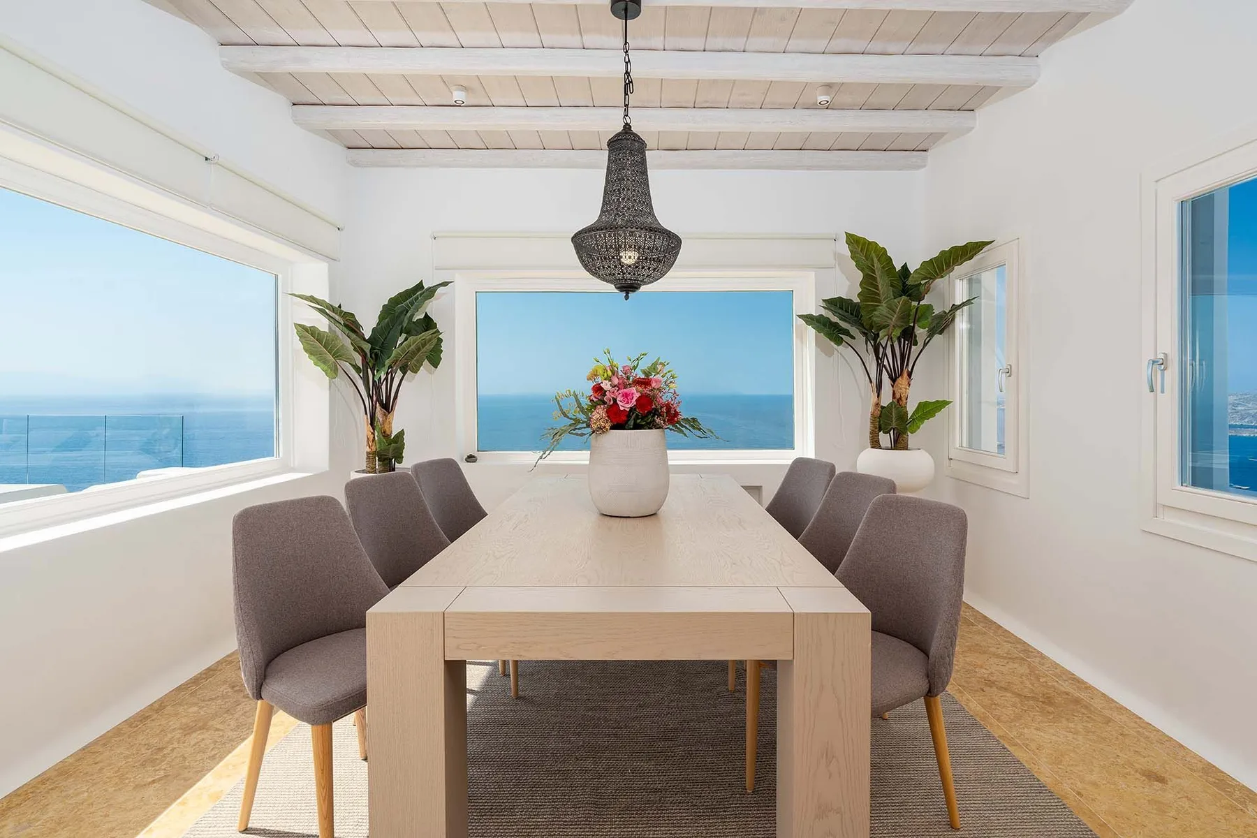 A bright dining room with a long table and ocean views through large windows.