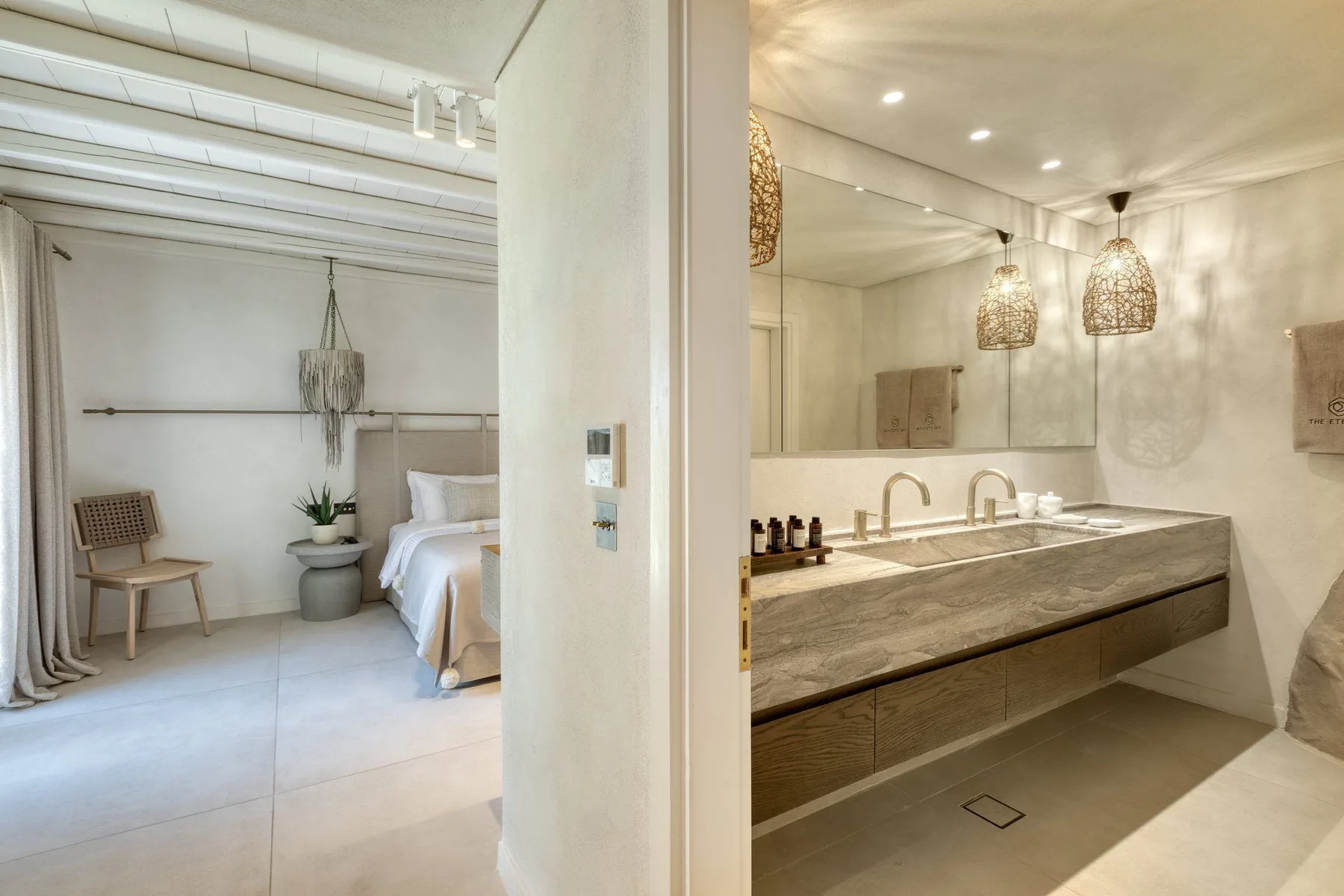 A bright bedroom opens onto a bathroom with a long vanity and mirror.