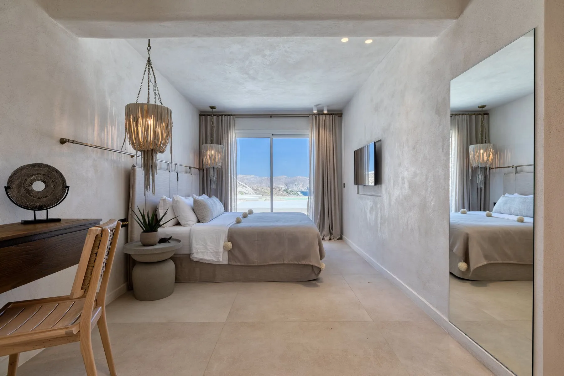 A bright bedroom with a bed, desk, and large window overlooking the water.