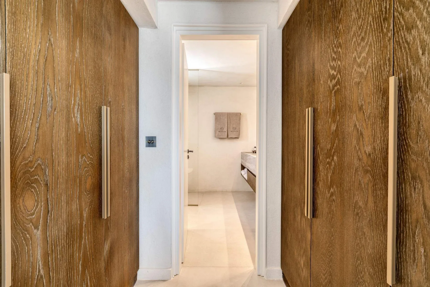 A hallway framed by wooden doors leads into a bright bedroom.