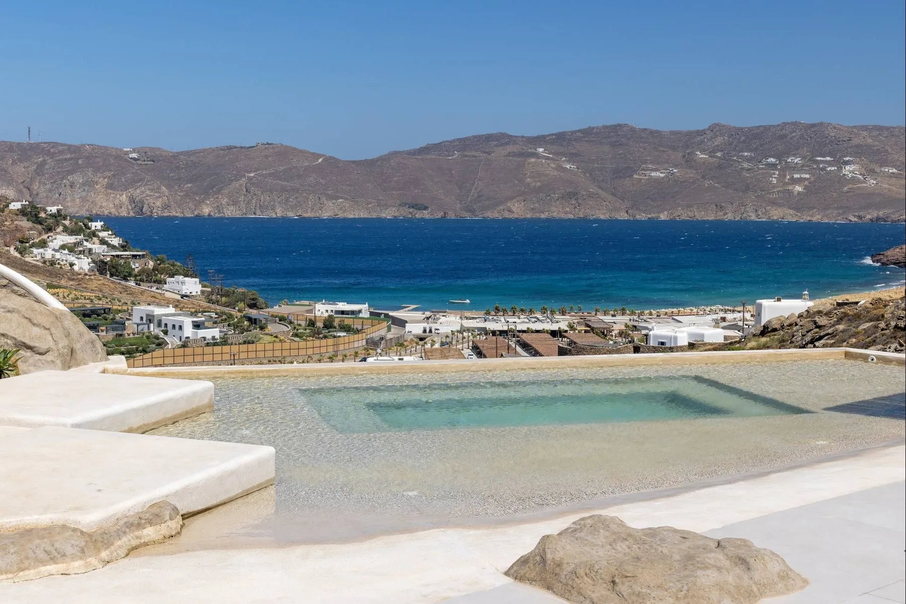 An outdoor pool overlooks a blue bay and the surrounding hills.