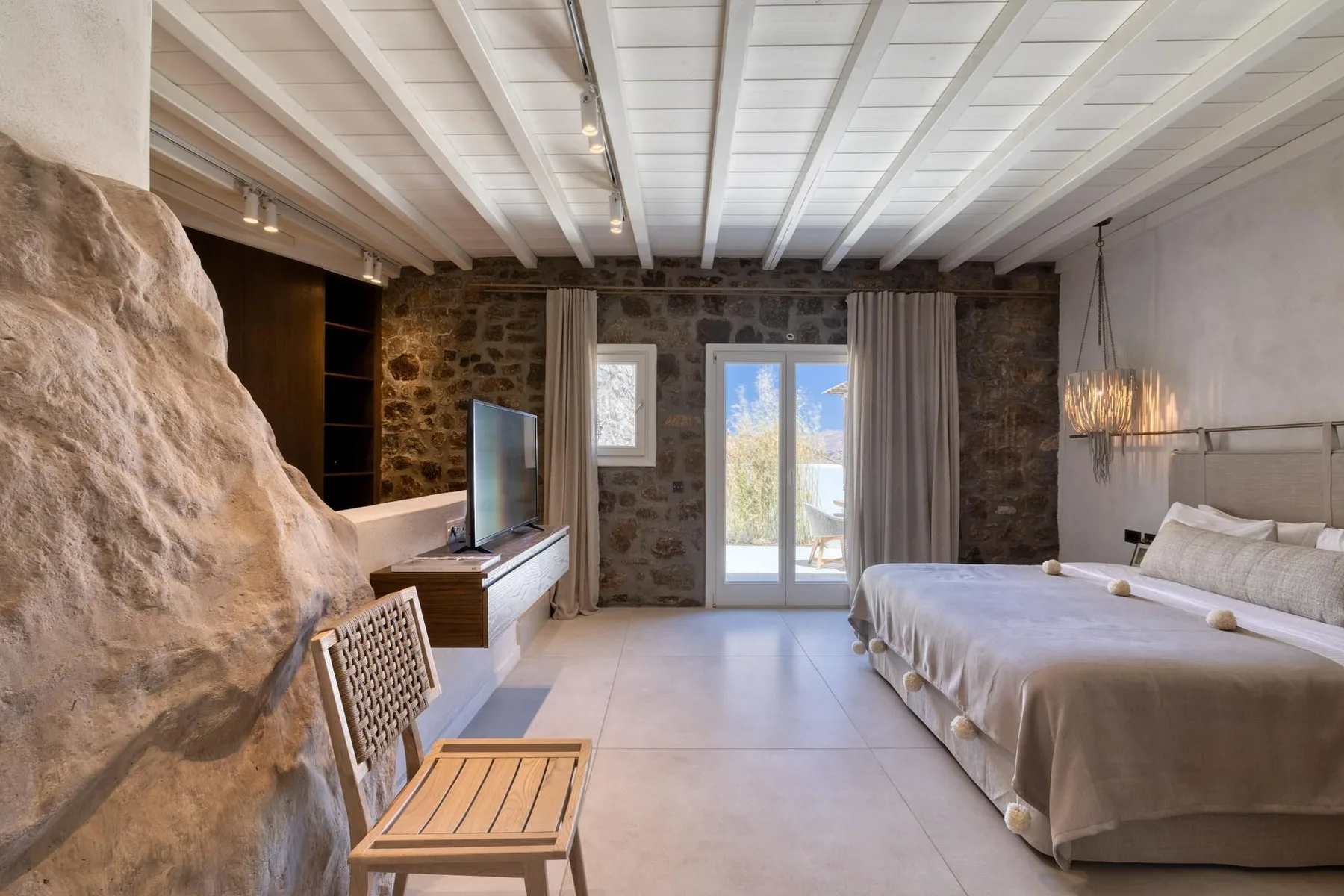 A bedroom with a bed, television, and glass doors opening to a balcony.