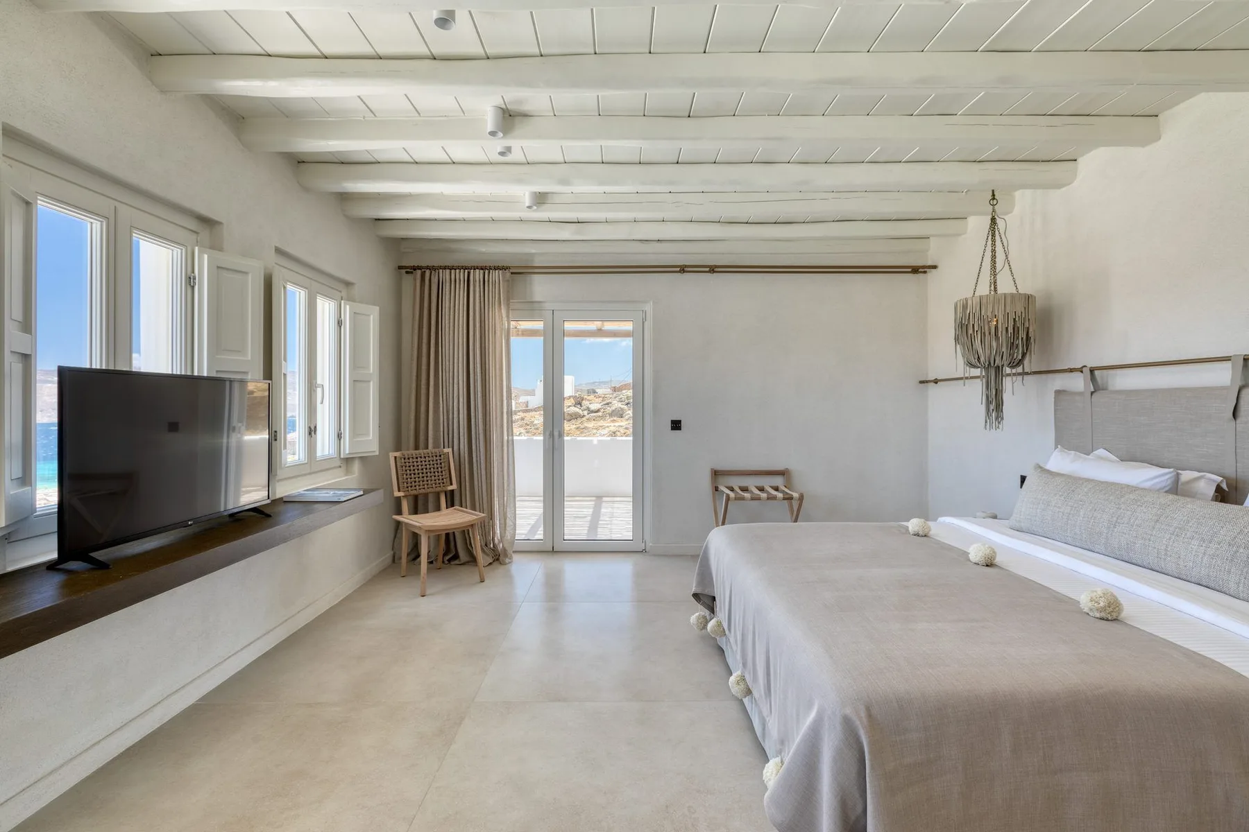 A bright bedroom with a large bed, television, and glass doors opening to a balcony.