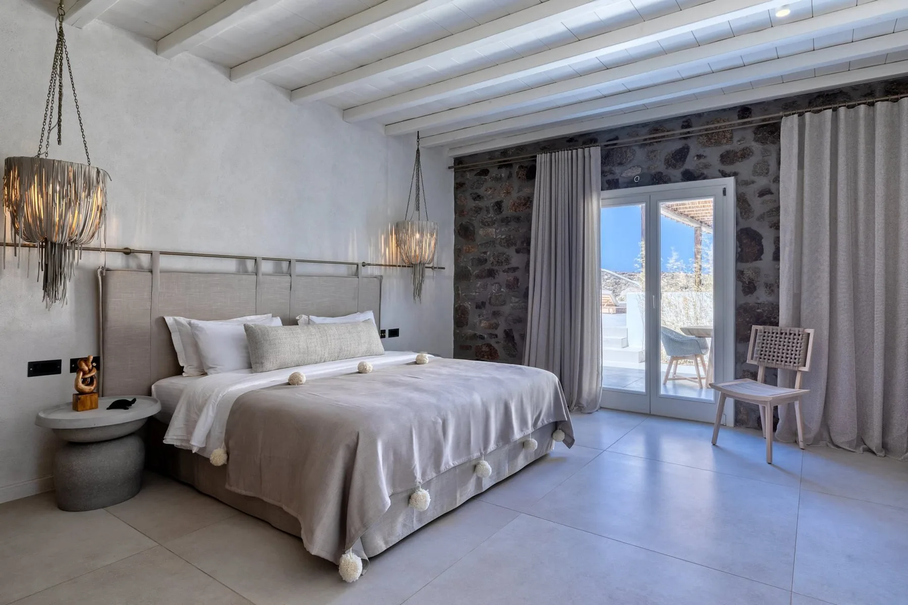 A bedroom with a bed, exposed ceiling beams, and glass doors opening to a balcony.