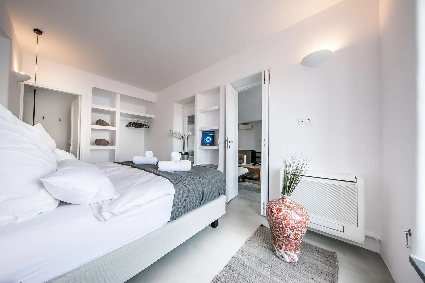 A bright bedroom with a neatly made bed and an open doorway.