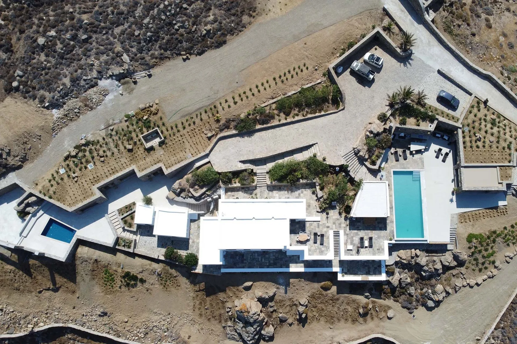 Aerial view of a large building and pool beside a rocky, landscaped hillside.