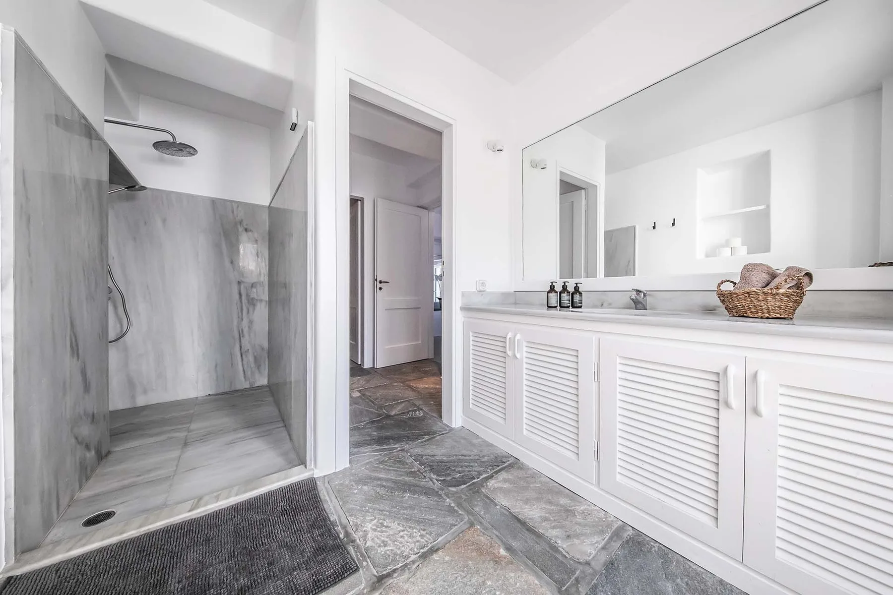 A bright bathroom with a glass shower, wide mirror, and white vanity.