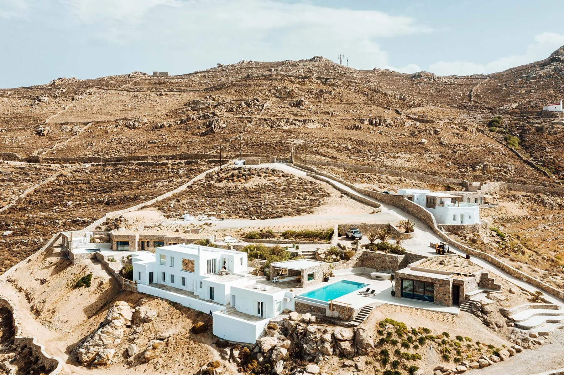 White buildings and a swimming pool sit among rocky hills.
