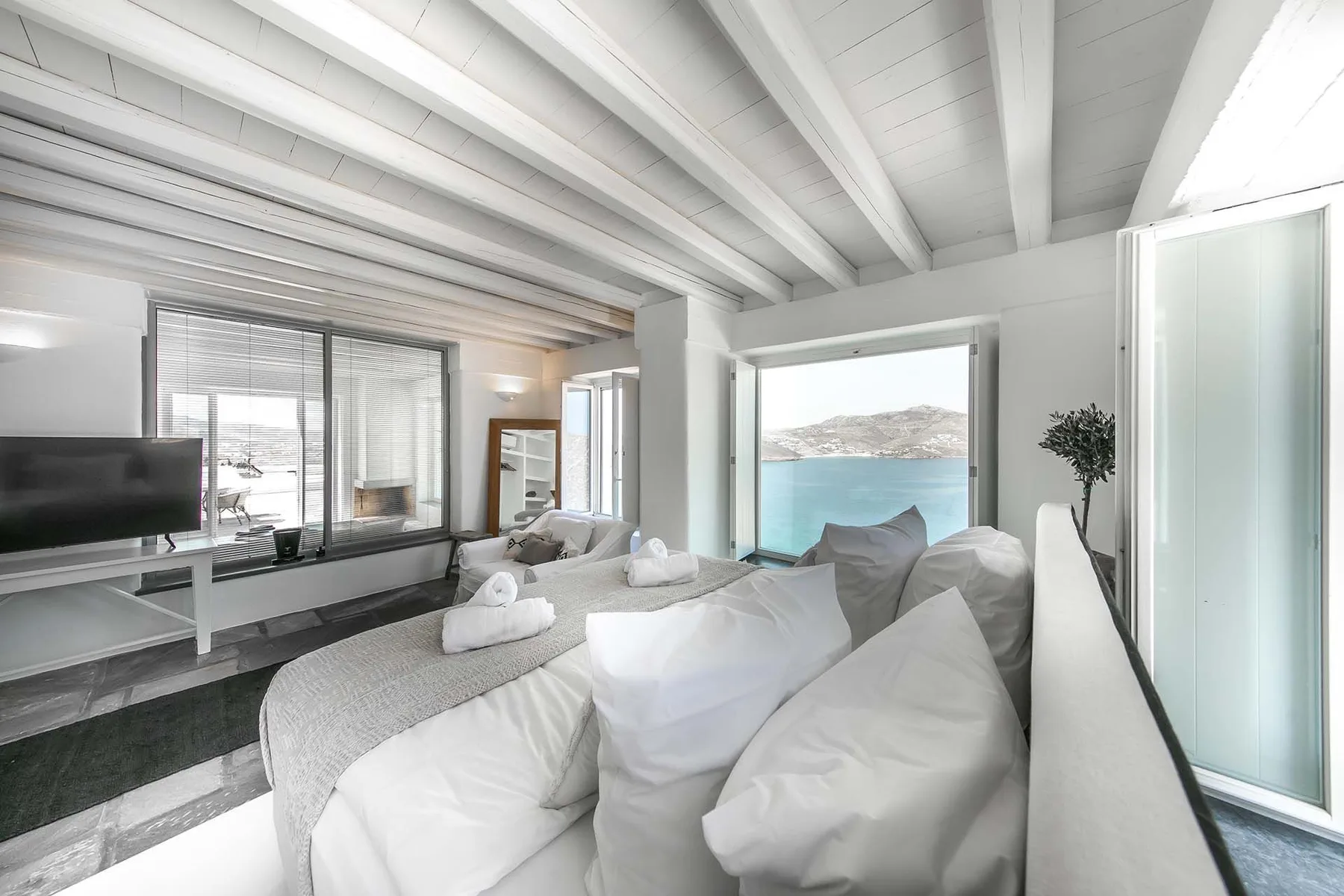 A bright living room with white seating facing a large window overlooking the water.