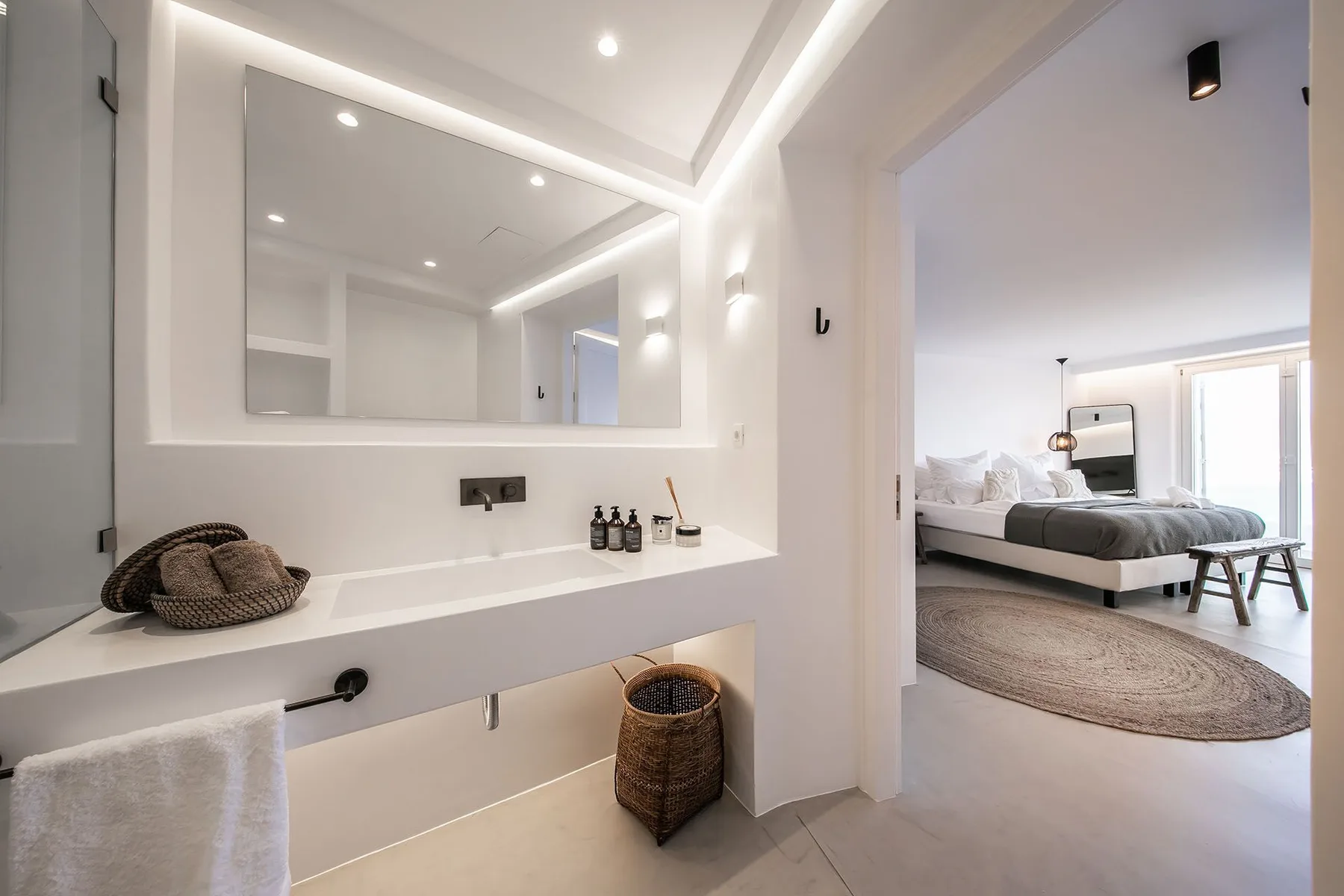 A bright bedroom with a large wall mirror and a bed visible through the doorway.