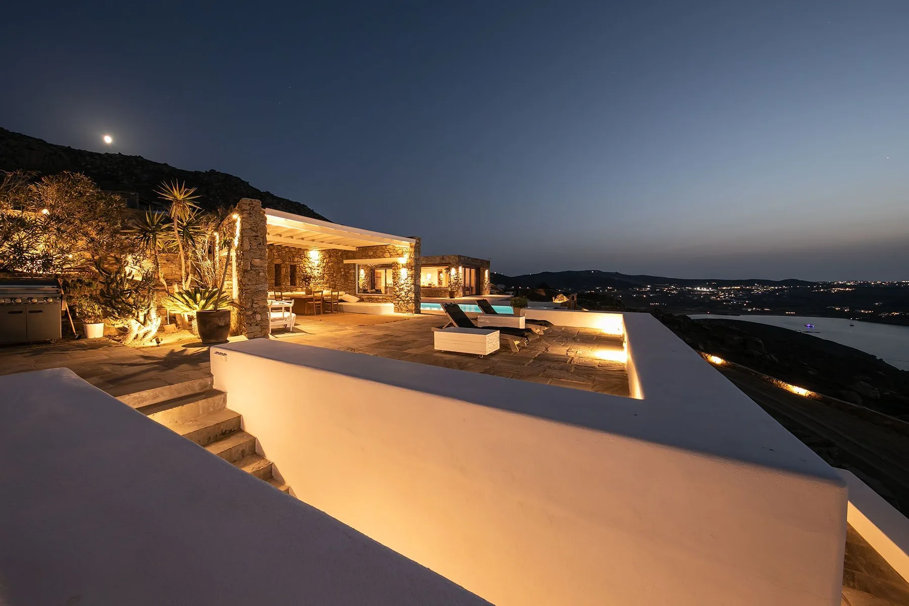 A modern outdoor terrace at dusk, with seating and an illuminated pool.