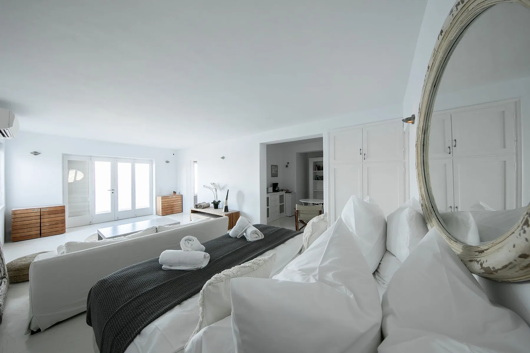 A bright bedroom with a large bed, dark runner, and tall windows.