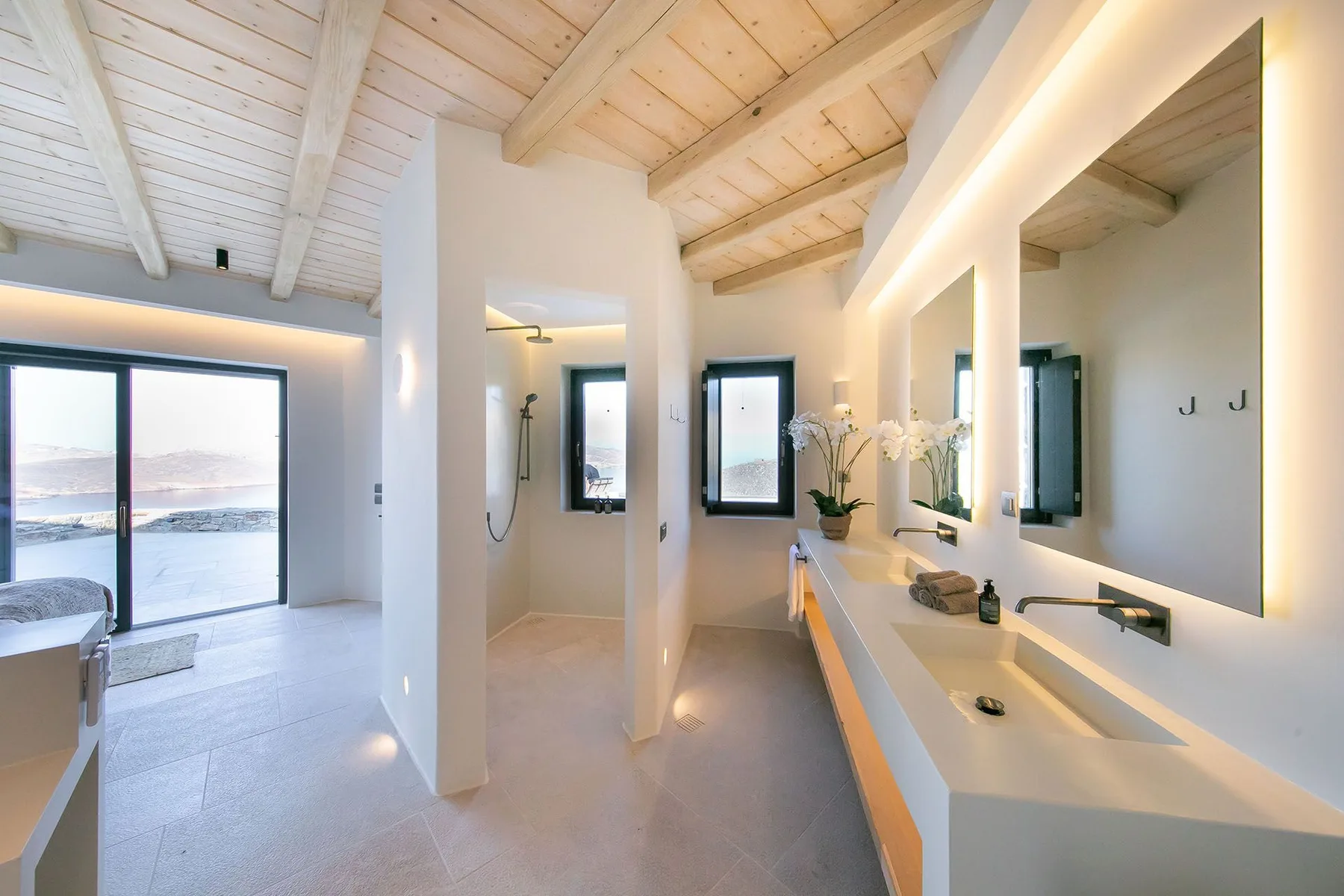 A bright bathroom with a long vanity, large mirrors, and a wooden ceiling.
