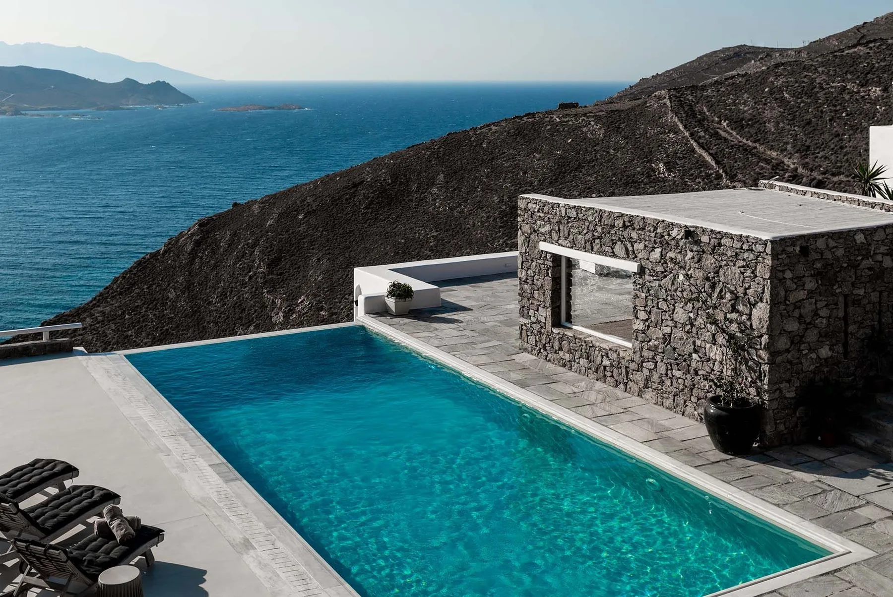 An outdoor swimming pool beside a stone building overlooks the sea.